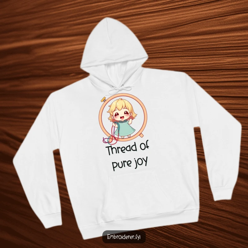 Funny hoodie showing a delighted character pulling a colorful thread from a giant embroidery hoop, cozy and creative.